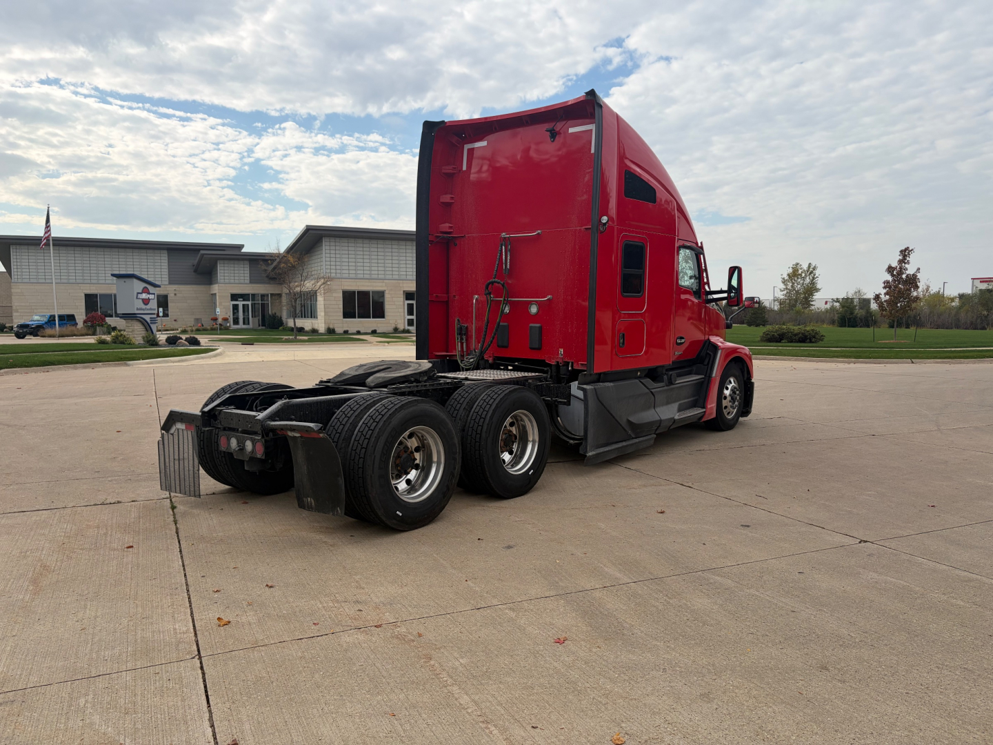 Kenworth T680 conventional sleeper tractor from rear-left side, red exterior, two rear axles, fifth wheel missing from view, clear sky.