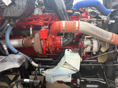 Kenworth T680 engine bay showing red engine block, large orange intake hose, blue silicone hose, coolant reservoir, and various components.