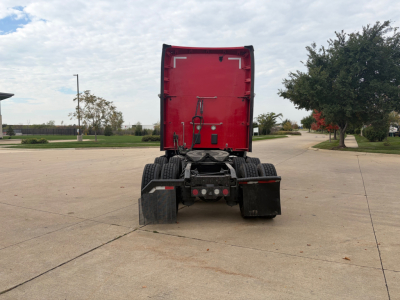 Kenworth T680 rear view showing fifth wheel and dual rear axles, red cab, trailer height clearance, clear sky.