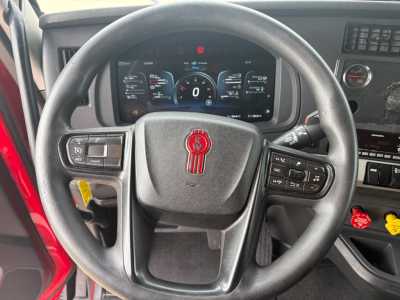Kenworth T680 dashboard and steering wheel with digital instrument cluster visible through steering wheel, showing steering wheel controls and interior switches.