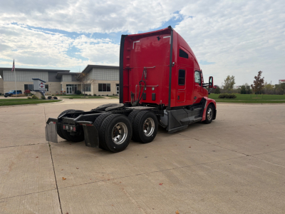 Kenworth T680 conventional sleeper tractor from rear-left side, red exterior, two rear axles, fifth wheel missing from view, clear sky.