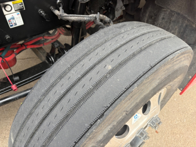 Kenworth T680 wheel/tire close-up showing front dual tread and hub area with suspension components nearby.