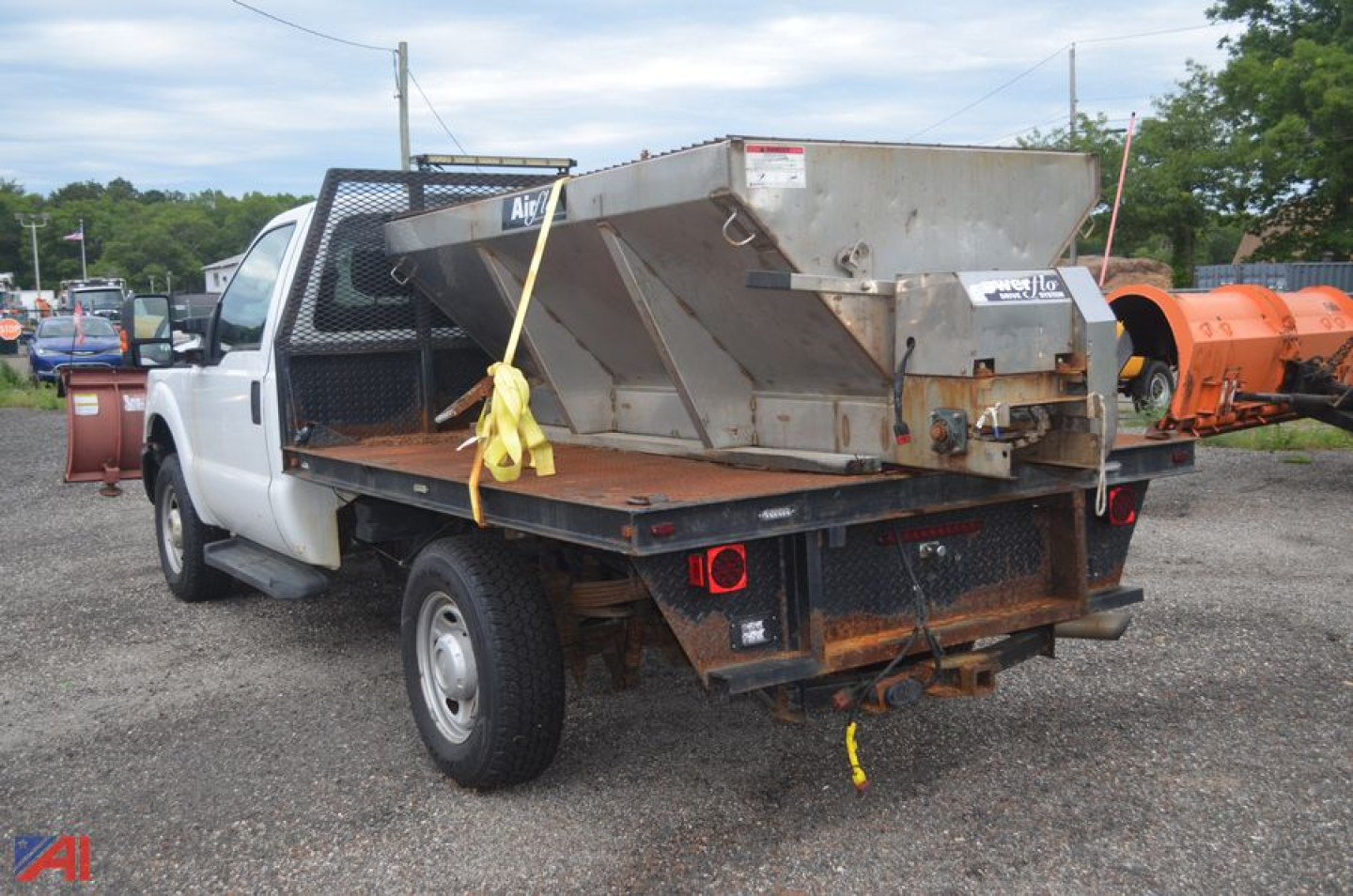 Ford F-250 Super Duty truck with flatbed and large spreader/plow equipment mounted in bed, rear view showing bumper and hitch.