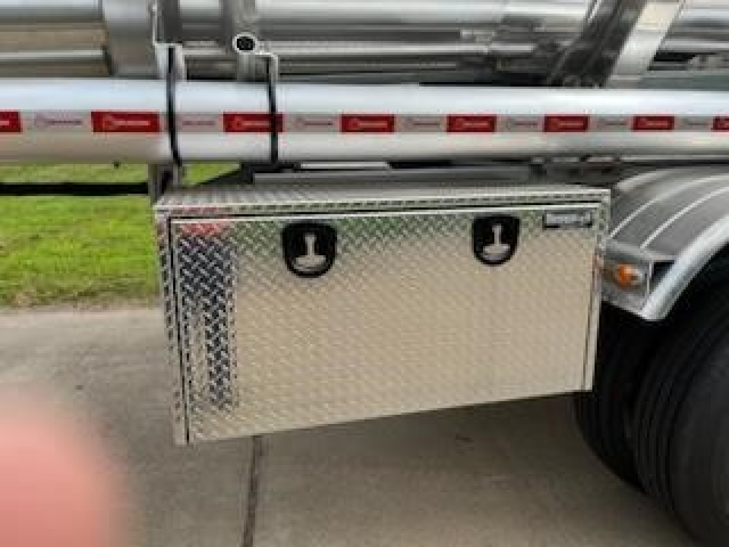 Trailer side box mounted under a stainless fuel/oil tank with diamond plate aluminum storage box and dual lid handles, thin red-and-white reflective tape on tank