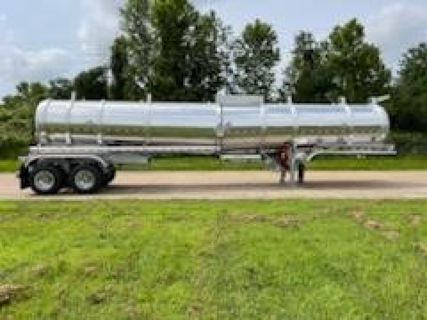Trailer tanker in-service showing cylindrical aluminum tank on tri-axle trailer with chrome fittings and supporting frame.
