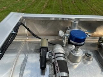 Trailer component showing fuel/pressure gauge, blue cap, and silver piping in a metal tank bed.