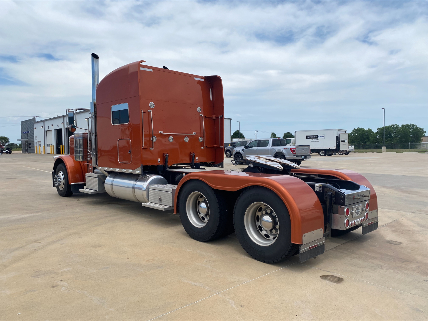 Peterbilt 389 tractor-trailer cab and rear dual axle from a side view with orange paint and chrome fuel tanks.