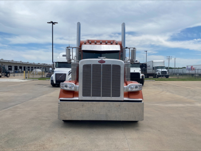 Peterbilt 389 front view showing large rectangular chrome grille with Peterbilt emblem, two tall chrome exhaust stacks, orange bumper area, and headlamps.