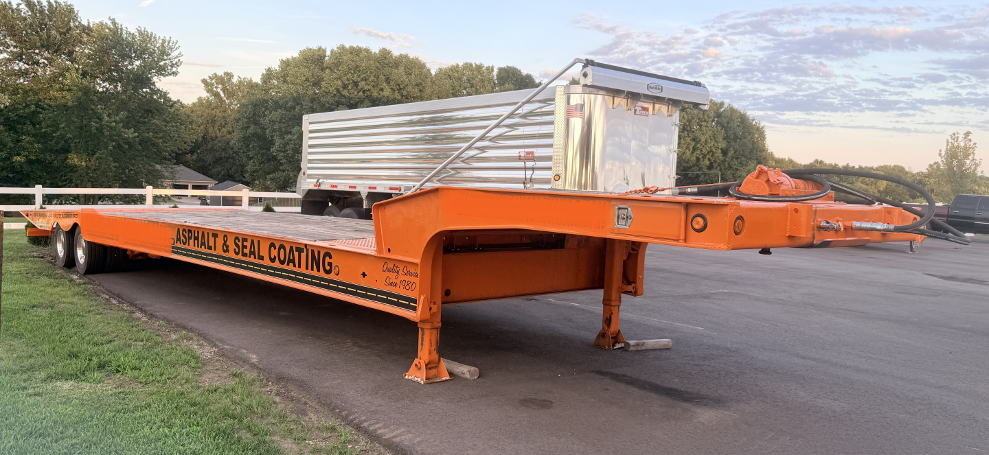 Orange Landoll lowboy trailer with ramp, dual axles, and a silver aluminum cargo trailer in background. Side text reads AS?PHALT & SEAL COATING.