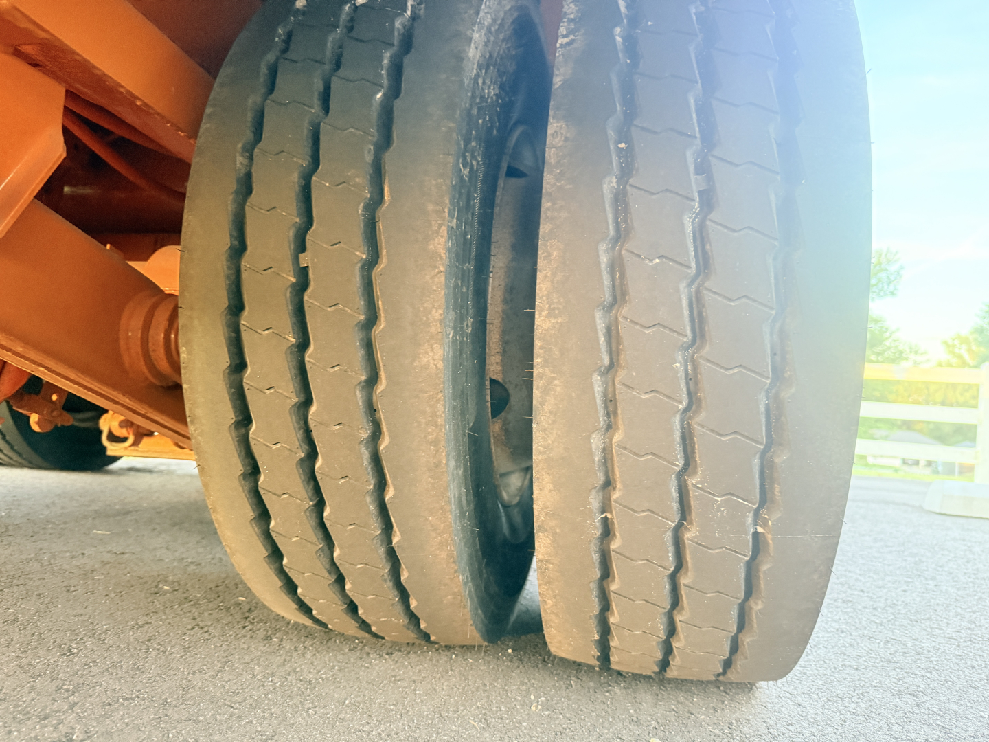 Dual rear tires of a lowboy trailer viewed close-up showing tread and inner wheel, orange frame visible.