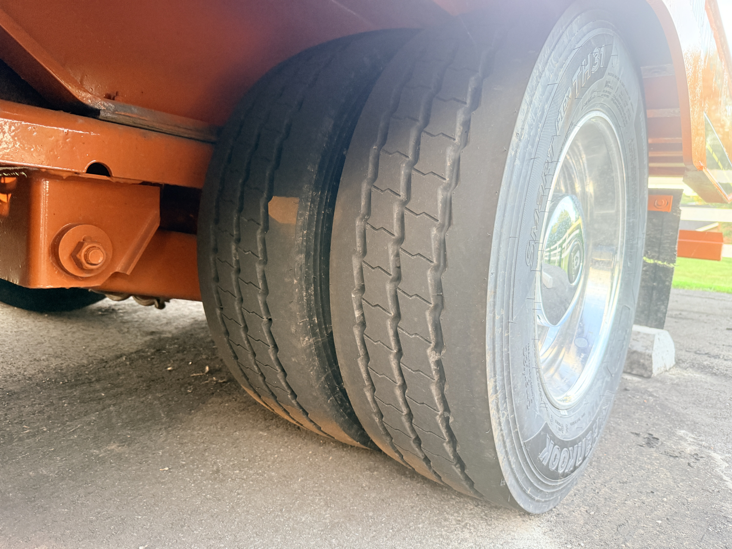 Lowboy trailer wheel and dual tires with orange chassis and bolt hardware visible.