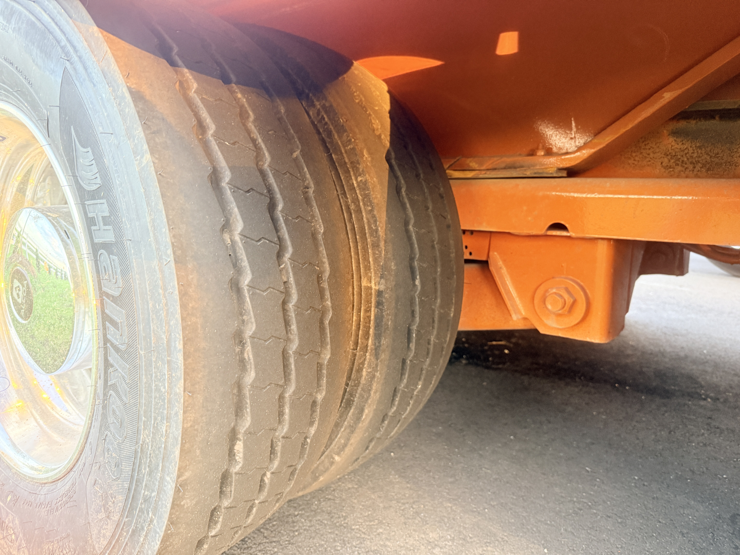 Trailer wheel and orange frame of a Landoll lowboy trailer showing dual tires and structural support. Visible text includes tire sidewall details.
