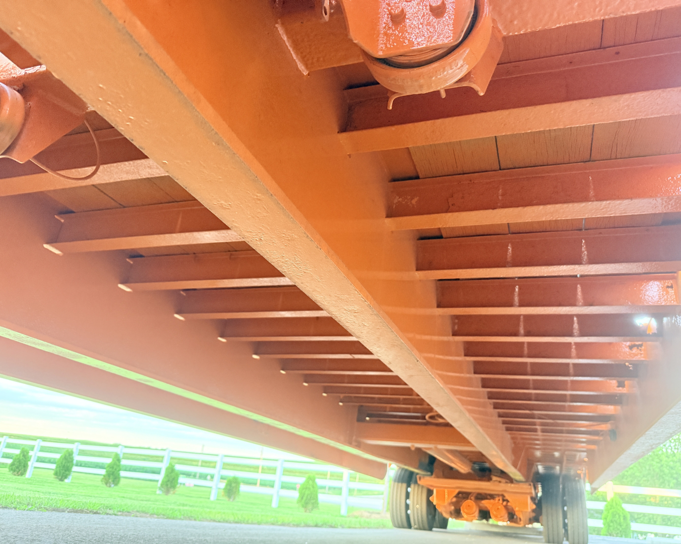 Traveling tail of a Landoll lowboy trailer showing orange-painted steel beams and wheel assembly undercarriage.
