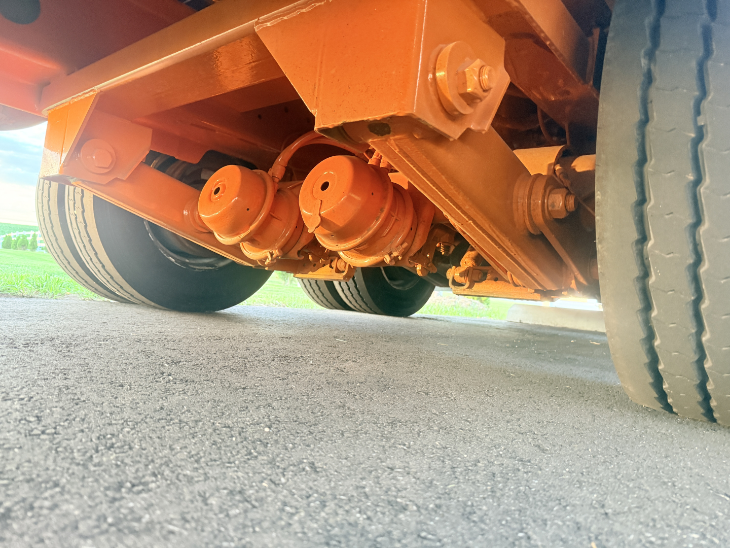 Low-angle underside view of a Landoll trailer showing orange-painted suspension components and wheels; undercarriage with visible rollers and axle hardware.