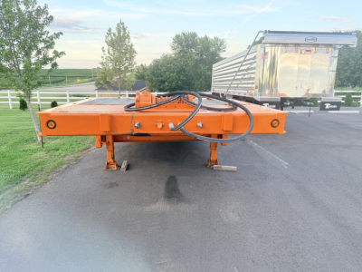 Traveling tail of a Landoll trailer in orange, with hydraulic hoses and mounting hardware visible on a flat pavement.