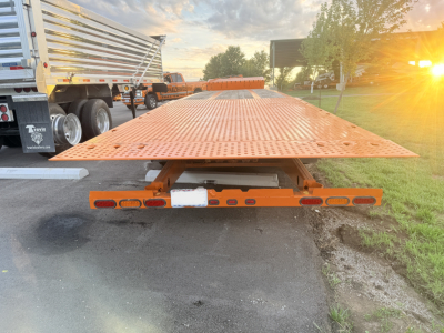 Traveling tail of a 2006 Landoll lowboy trailer with orange perforated deck and rear lighting, view from behind; VIN tag and stock number visible.