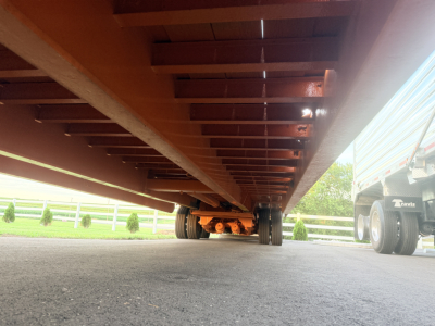 Bottom view of a traveling tail trailer with orange undercarriage and wheels, showing underside and suspension components.