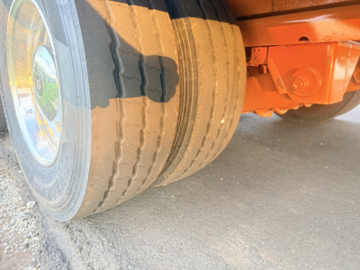 Wheel and undercarriage of a lowboy trailer with orange frame and dual rear wheels; no legible labels visible in this photo.