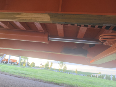 Rail/undercarriage view of a Landoll trailer showing a cylindrical cylinder/piston component under the frame and structural crossmembers.