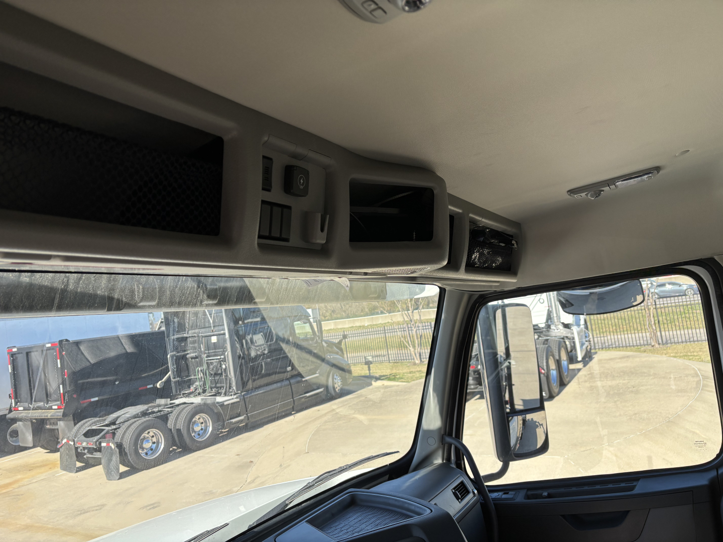 Truck cab interior with overhead control panels and a window showing a dealership lot with other trucks.