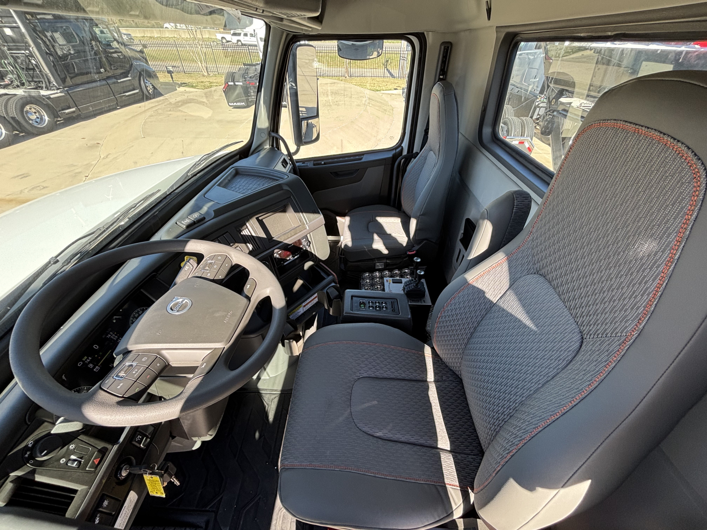 Volvo VHD64B300 cab interior showing steering wheel, driver seat, dashboard, center console with controls, and passenger seat.