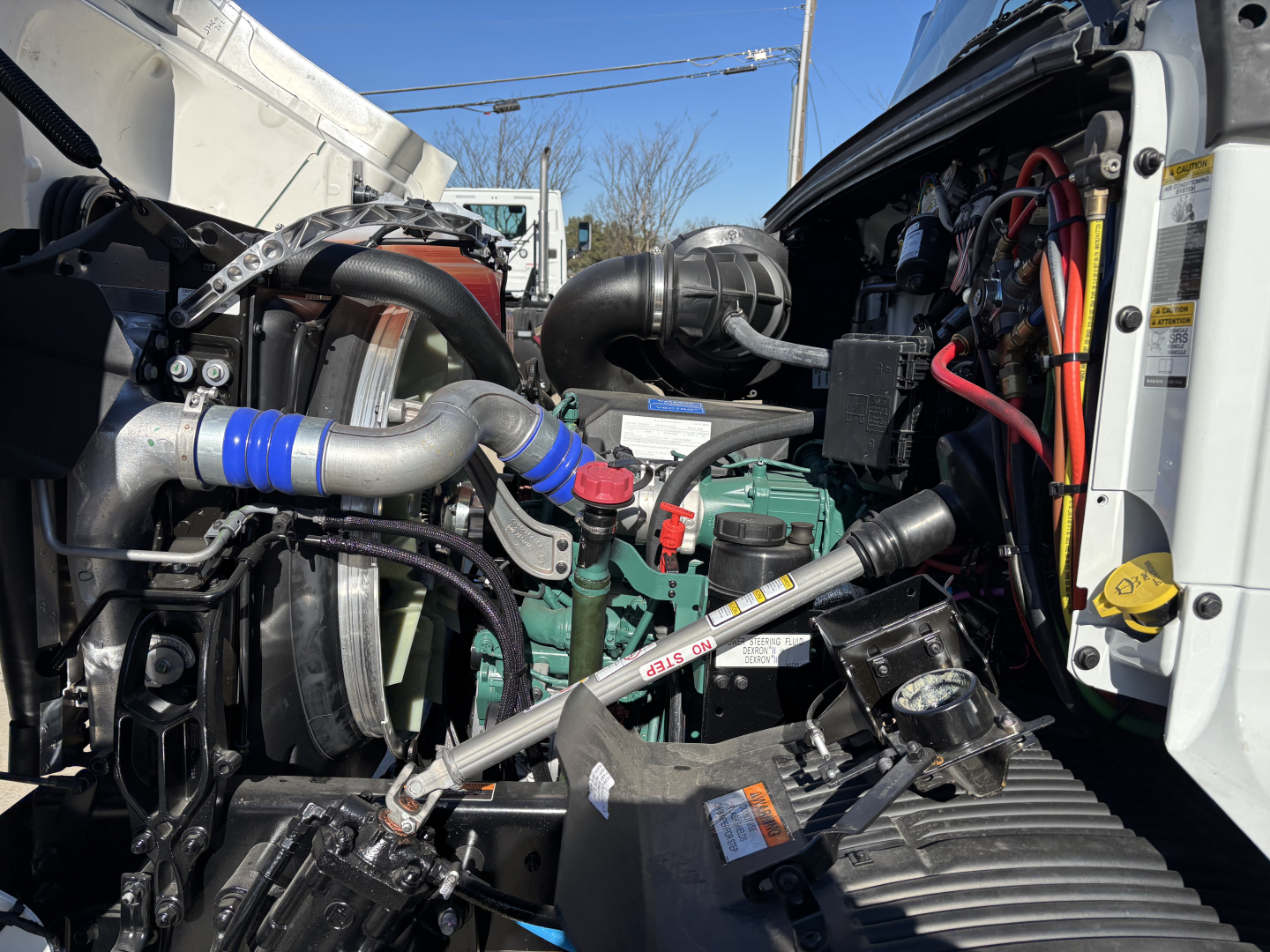 Volvo VHD64B300 engine bay showing coolant hoses, air intake, radiator, and hydraulic lines with blue silicone hose clamp.