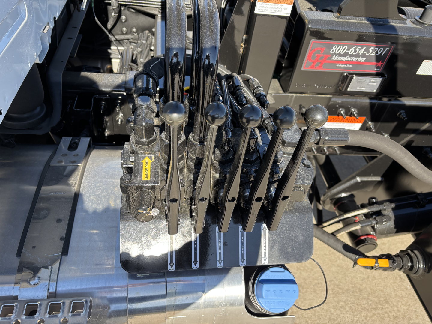 Lever controls and hydraulic levers in a Volvo VHD64B300 roll-off truck cab area showing multiple black toggle levers and a blue cap on a hydraulic reservoir.
