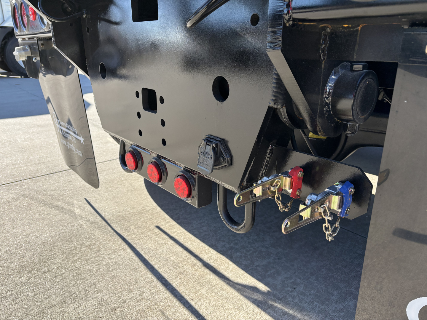 Volvo VHD64B300 roll-off truck rear chassis showing hitch, hydraulic lines, and safety latches with red/blue components and chain attachments.