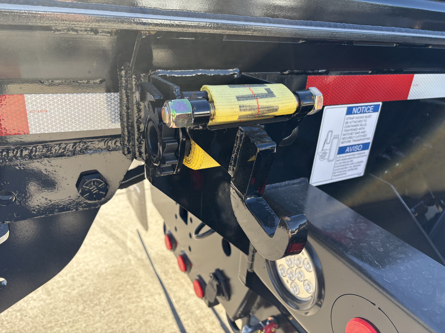 Trailer hitch area of a new Volvo VHD64B300 rolloff truck showing a safety pin and latch with a yellow warning tag, side reflector, and sticker panel.