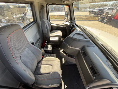 Cab interior of a new Volvo VHD64B300 rolloff truck showing steering wheel, driver seat, passenger seat, dashboard, center console, and window view.