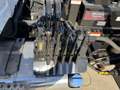Lever controls and hydraulic levers in a Volvo VHD64B300 roll-off truck cab area showing multiple black toggle levers and a blue cap on a hydraulic reservoir.