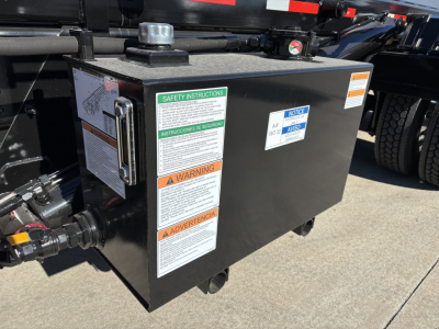 Rolloff truck component with safety instruction labels and warning stickers on a black metal box attached to a Volvo VHD64B300 chassis.
