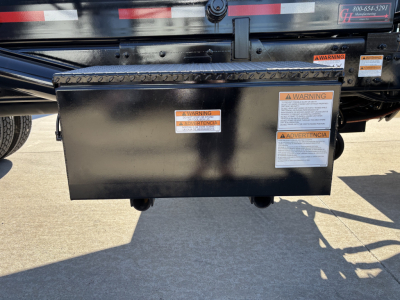 Rolloff truck side toolbox mounted under bed with warning labels and stickers visible on black metal box.