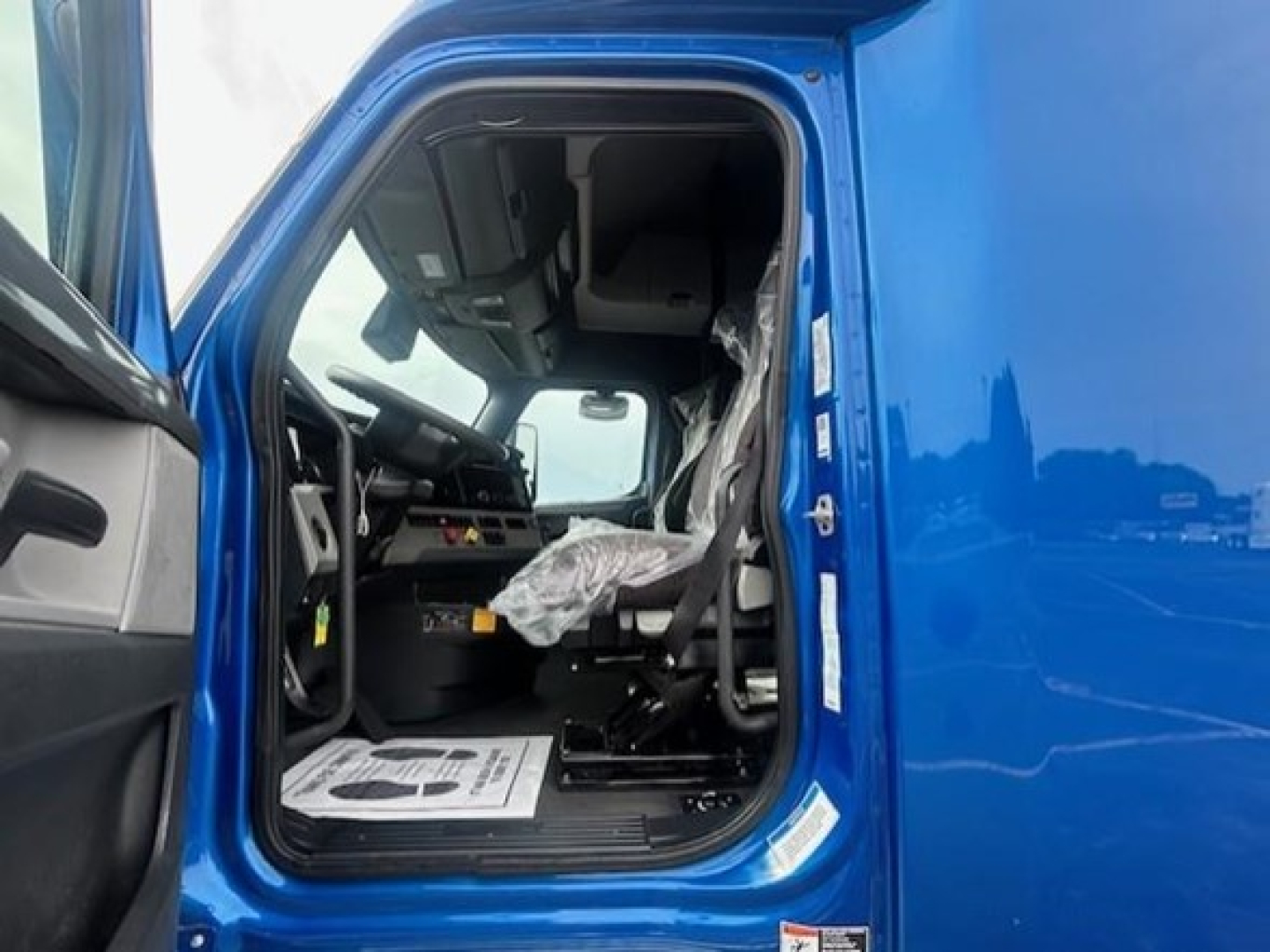 Truck cab interior of a 2022 Freightliner Cascadia 126, blue exterior, open driver door showing seat and dashboard.