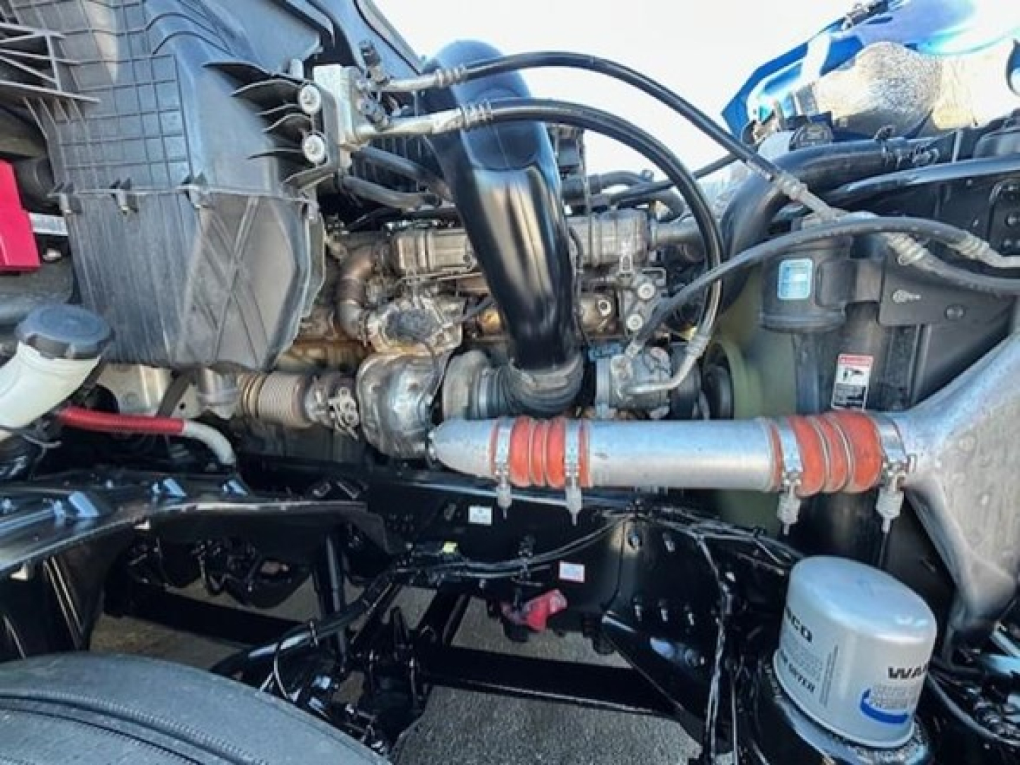 Freightliner Cascadia engine bay showing diesel engine, intake, hoses, and coolant reservoir; view from side with front axle and components visible.