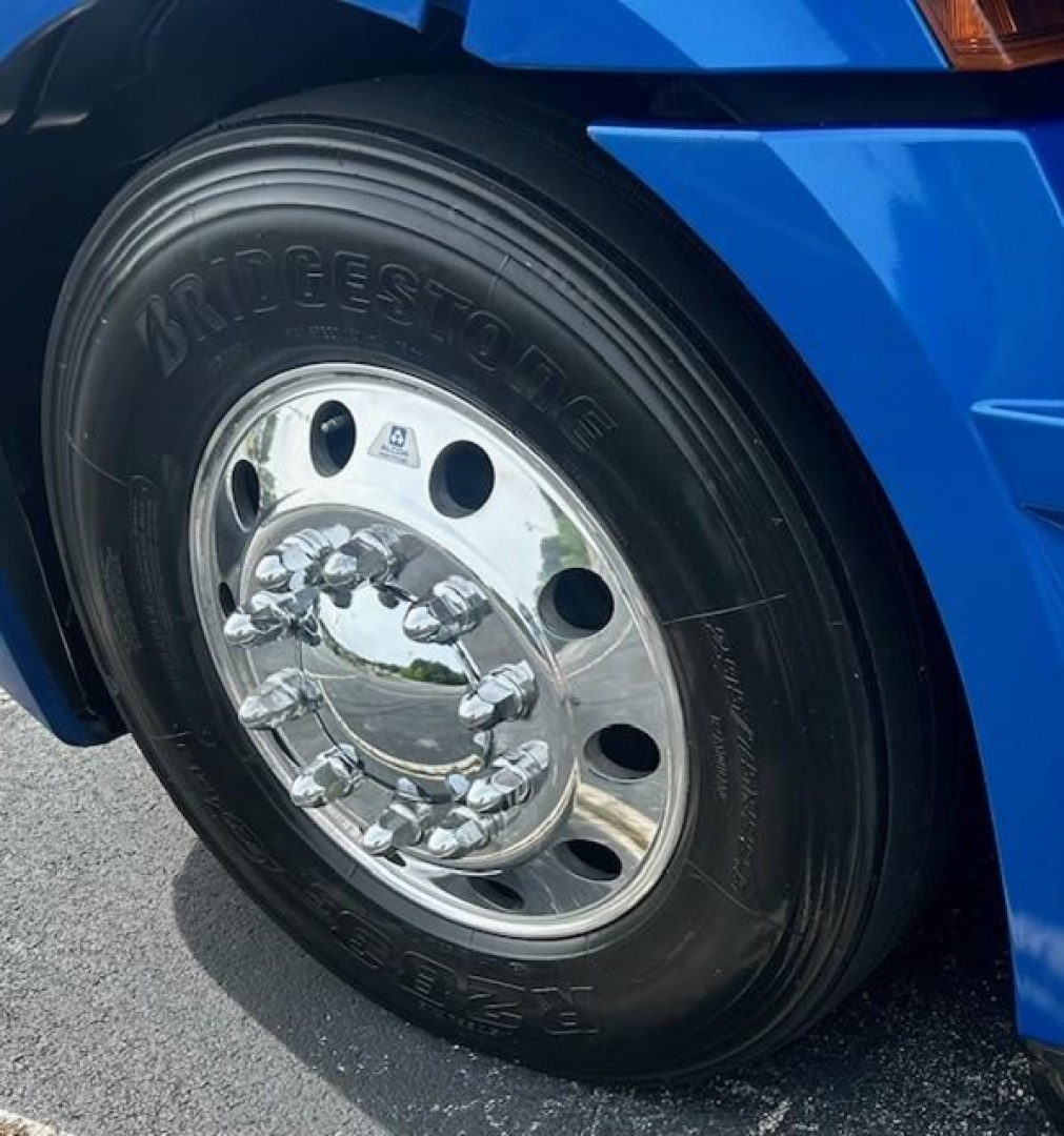 Bridgestone tire and chrome wheel on blue Freightliner Cascadia front axle, partial fender and wheel well visible.