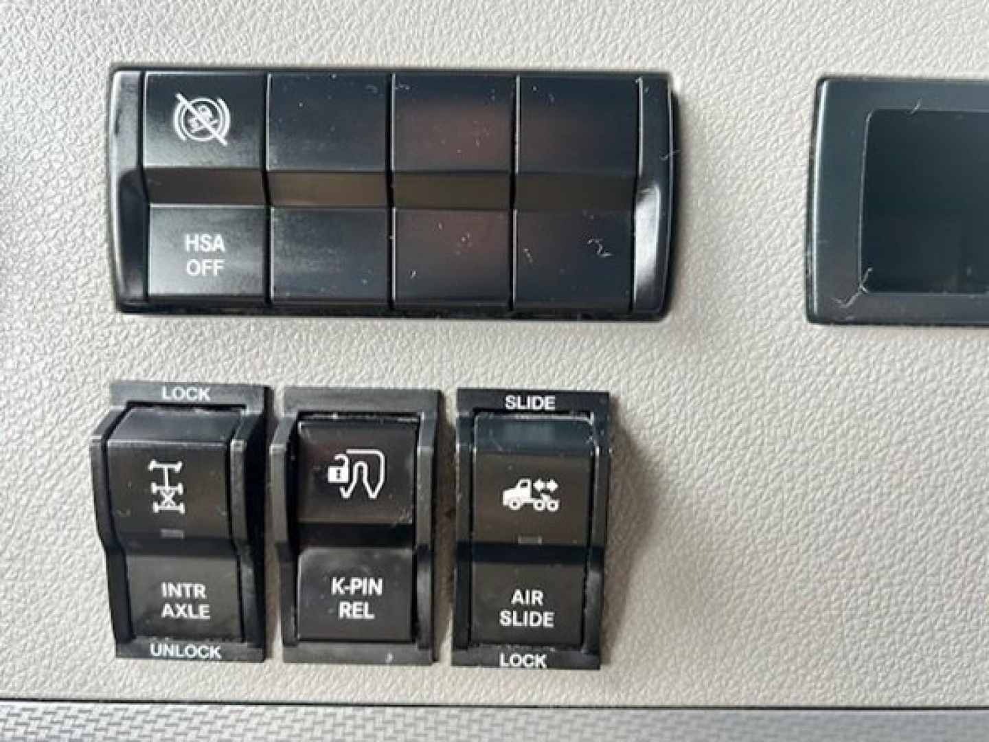Dashboard switches and controls on Freightliner Cascadia interior showing HSA OFF, lock/unlock, slide, intraxle, k-pin relay, air slide switches.