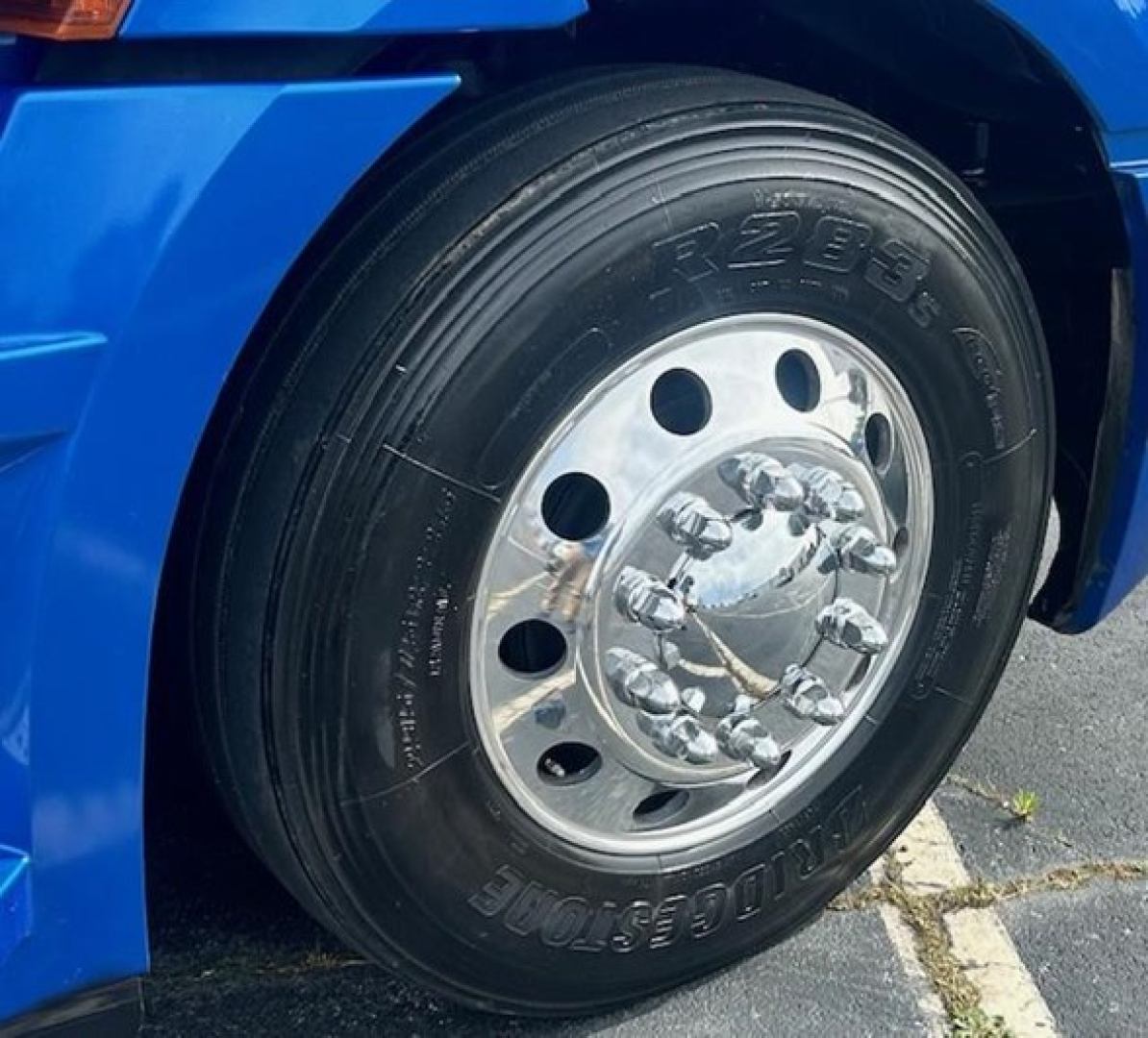 Front wheel of blue Freightliner Cascadia 126 showing heavy-duty tire and polished chrome hub with lug nuts.