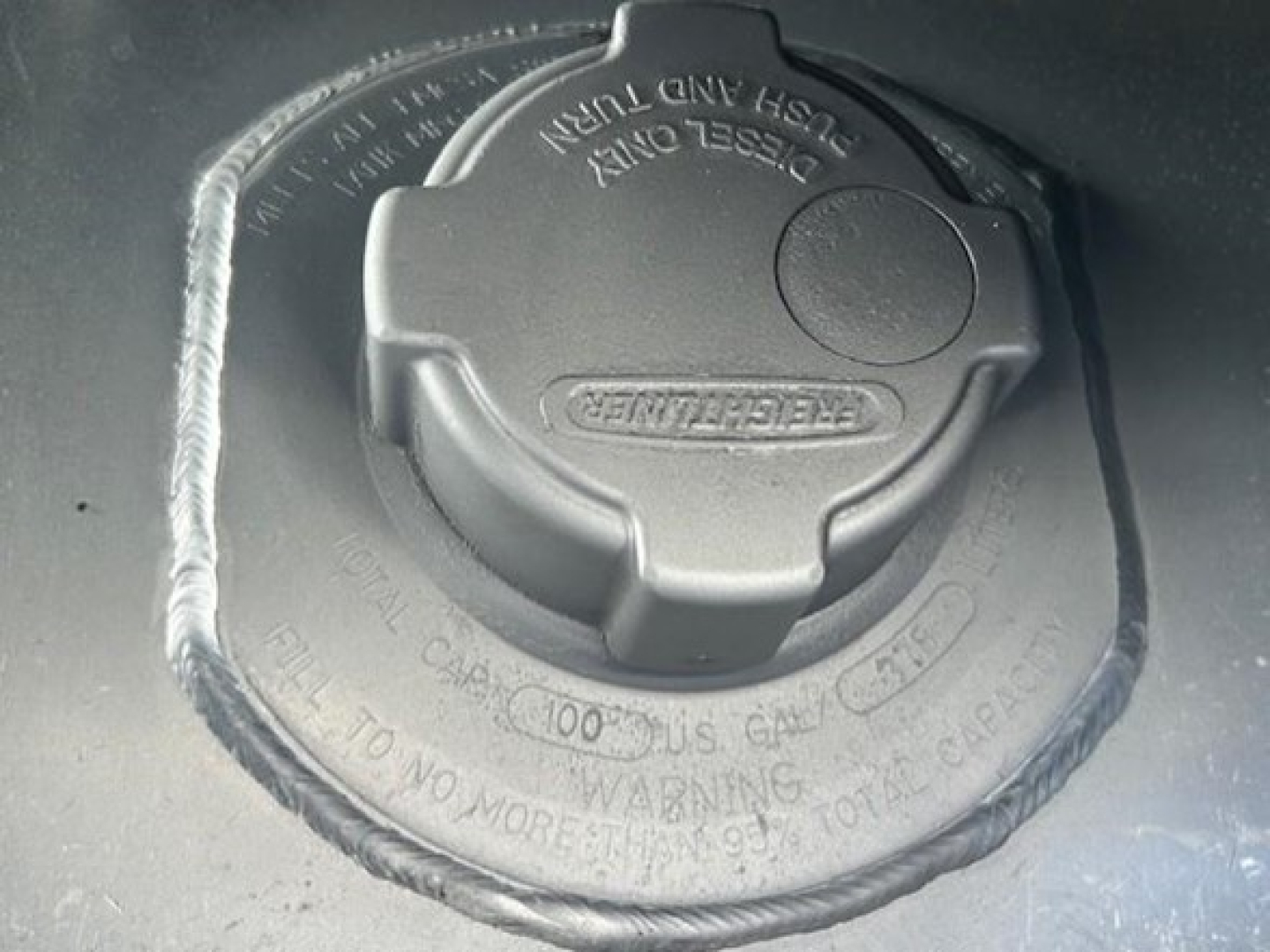 Fuel tank cap and surrounding area on Freightliner Cascadia engine bay showing fuel filler cap and adjacent warning text.