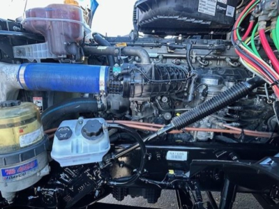 Freightliner Cascadia 126 engine bay showing top of engine with blue radiator hose, coolant reservoir, air filter canister, and wiring harnesses.