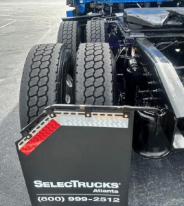 Rear axle and dual tires of a Freightliner Cascadia truck showing fender, chassis, and access steps with SelectTrucks Atlanta branding plate.
