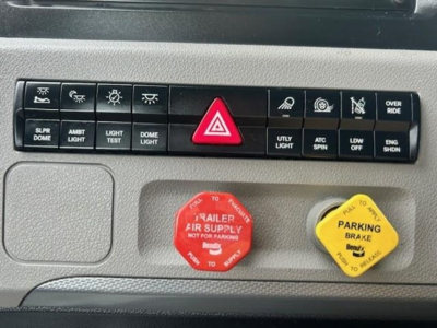 Freightliner Cascadia dash controls showing red trailer air supply knob and yellow parking brake knob with warning texts.