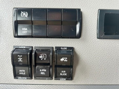 Dashboard switches and controls on Freightliner Cascadia interior showing HSA OFF, lock/unlock, slide, intraxle, k-pin relay, air slide switches.