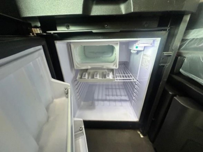 Small fridge/freezer in truck cab with open door and empty interior, showing shelves and freezer compartment.