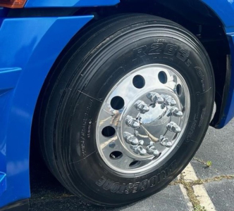 Front wheel of blue Freightliner Cascadia 126 showing heavy-duty tire and polished chrome hub with lug nuts.