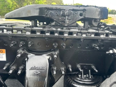 Truck cab mount showing Freightliner/Detroit engine components with a HACKER/landing pad, multiple bolts, and a label area. Text visible includes 'IN' on a small plate and generic hardware.