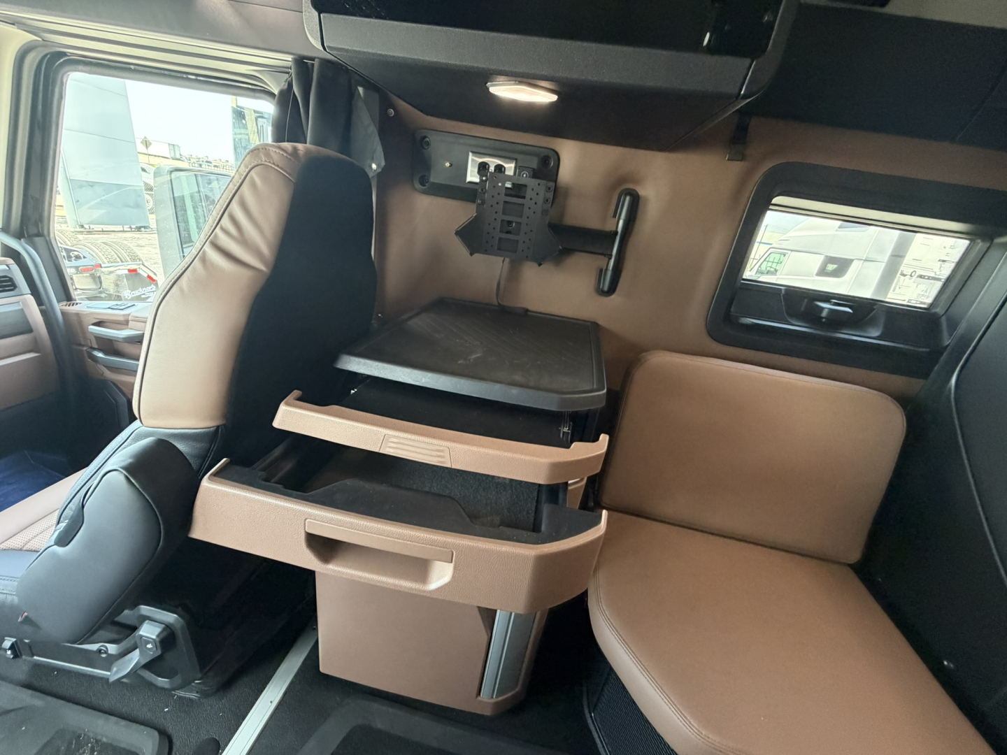 Front interior cab of a new Mack PR64T76H showing a brown leather sleeper seating area with flip-down tray and storage drawers.