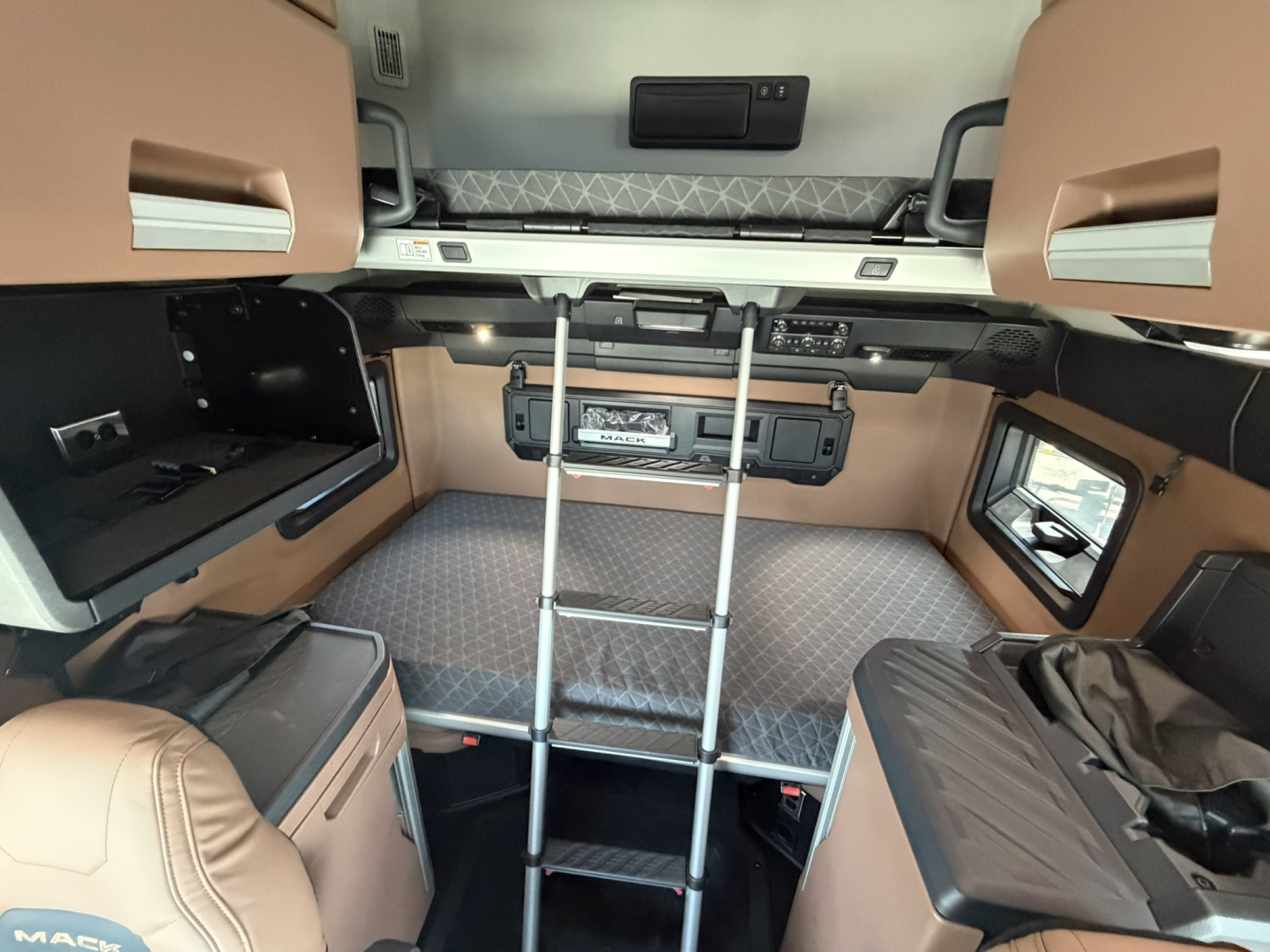 Interior of a new 2027 Mack PR64T76H sleeper cab showing bunk area, ladder, and side cabinets.