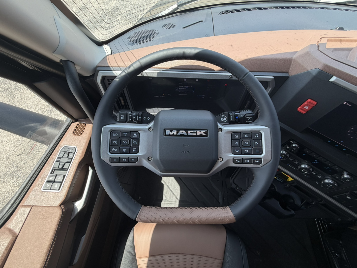 Interior view of a Mack PR64T76H truck dashboard and steering wheel showing the Mack logo on the center, left and right control panels, and dashboard gauges.