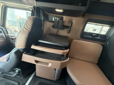 Front interior cab of a new Mack PR64T76H showing a brown leather sleeper seating area with flip-down tray and storage drawers.